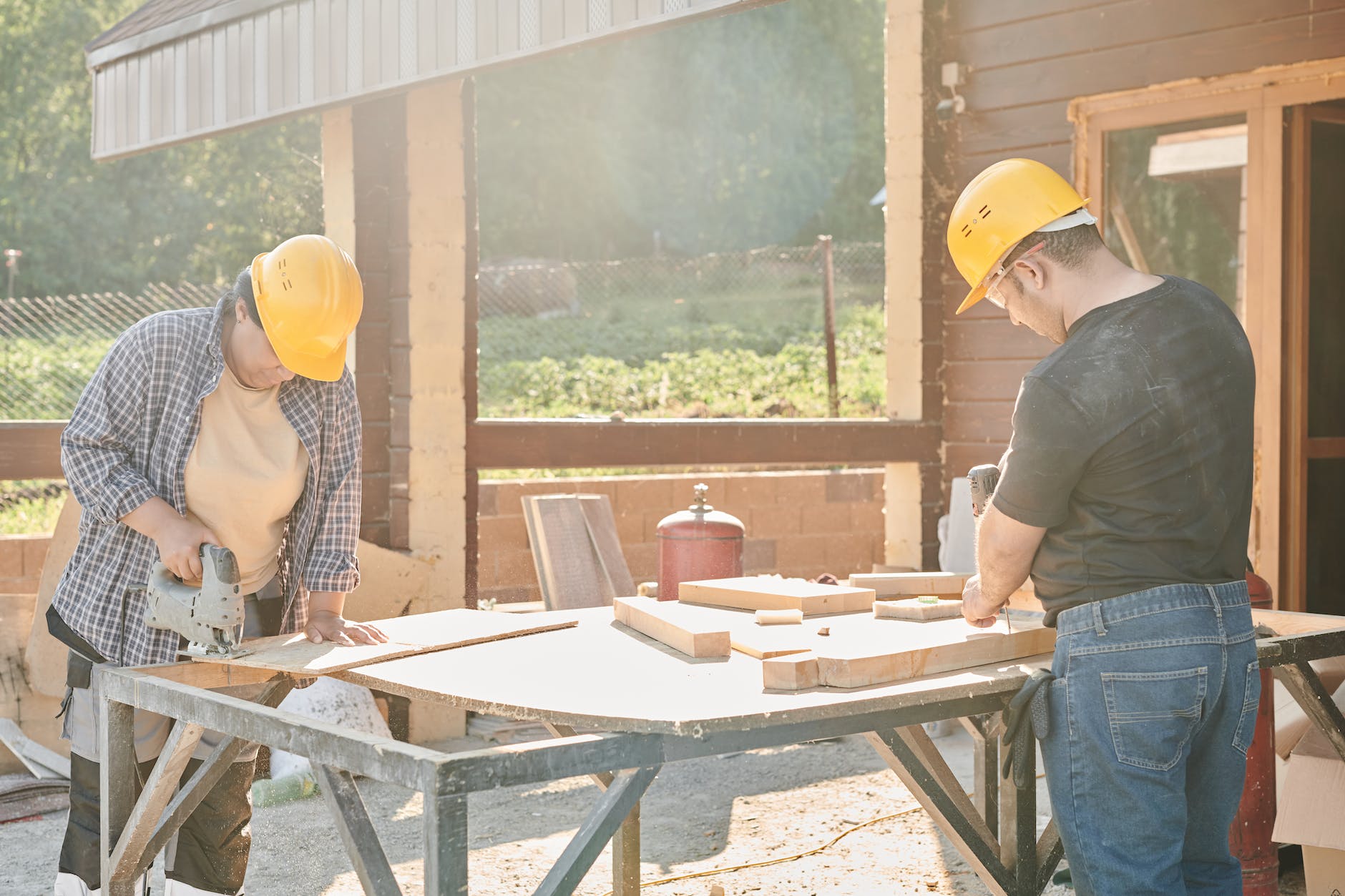 man and woman in yellow hard hats working using industrial tools